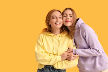 Fototapeta premium Beautiful young woman hugging her mother on yellow background. International Hug Day