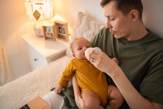 Father feeding newborn baby with formula at home
