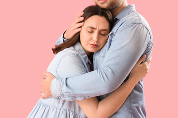 Sad young woman hugging her husband on pink background, closeup
