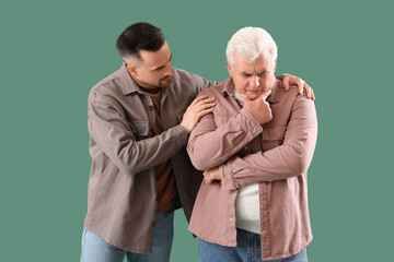 Young man calming his upset father on green background