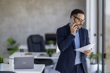 Businessman Discussing Documents on Phone in Modern Office