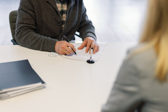 Man seated at desk in office signing contract in presence of manager