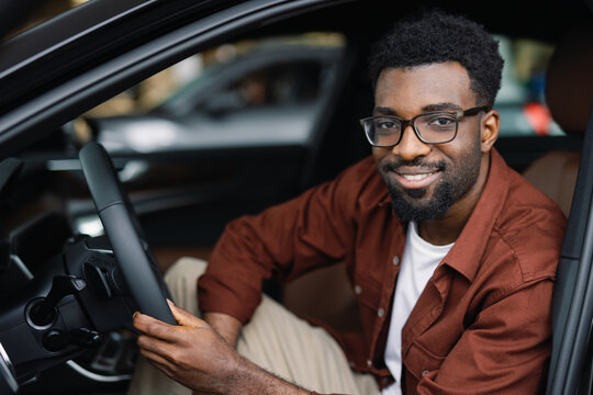 Joyous auto dealership customer posing behind wheel of motor vehicle