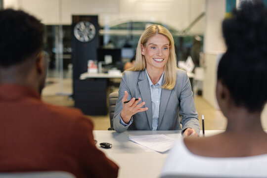 Manager communicating with couple of clients in car dealership office