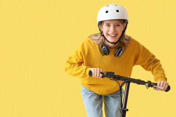 Beautiful young woman in helmet with modern electric kick scooter on yellow background