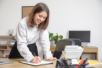 Pretty businesswoman writing on clipboard at table in light office