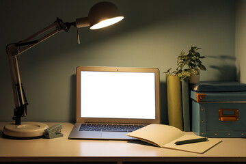 Workplace with modern laptop and glowing lamp near green wall
