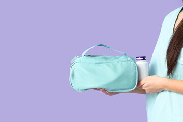 Female doctor with first aid kit and jar of pills on lilac background