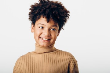 Young african american girl with curly hair in tan turtleneck sweater against a white background, radiating confidence