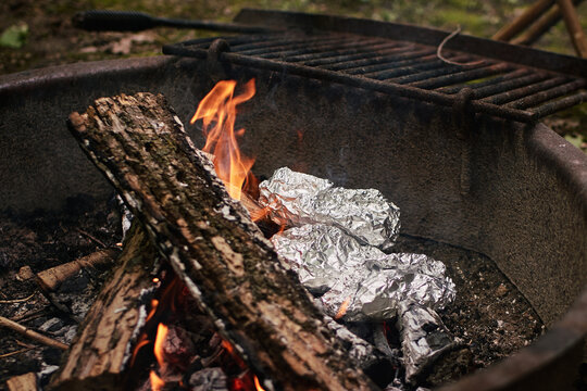 Foil-wrapped meals cooking in campfire flames
