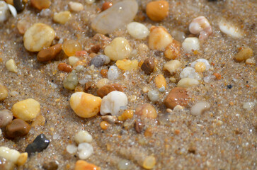 Lots of tumbled rocks on a sandy beach with water close up