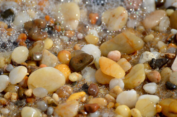 Lots of tumbled rocks on a sandy beach with water close up
