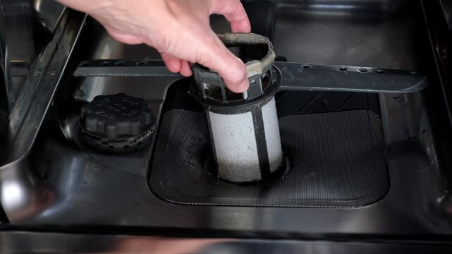 A hand taking out dishwasher filter to clean it, dis washer cleaning concept, kitchen home appliances care and maintenance