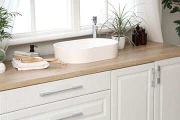 Fototapeta premium Modern sink, towels and massage body brushes on chest of drawers near window in bathroom