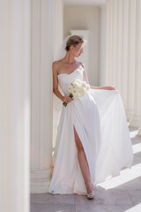 Fototapeta premium A beautiful bride in a white dress with a bouquet of white flowers on a light background. The year of the family. Marriage