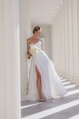 Fototapeta premium A beautiful bride in a white dress with a bouquet of white flowers on a light background. The year of the family. Marriage