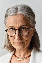 Fototapeta premium A beautiful mature woman showcases her style and confidence in a chic white suit against a grey background.