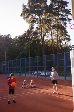 Schoolboy making basketball set shot under supervision of PE teacher