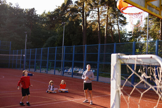 Pupils learning to throw basketball into basket supervised by coach