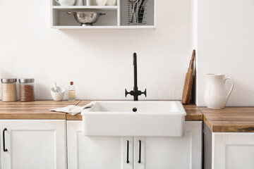 Fototapeta premium Sink on wooden counter near white wall in light kitchen