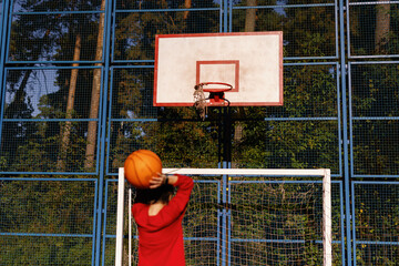 Kid throwing ball into basketball hoop on  outdoor playground in park