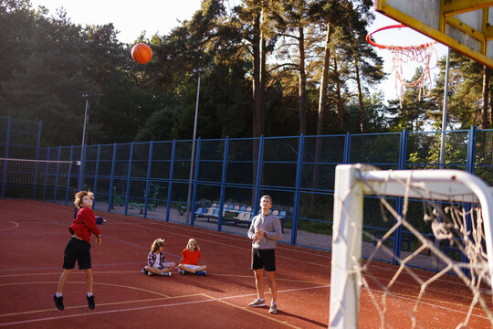 Pupil making basketball jump shot under supervision of PE teacher