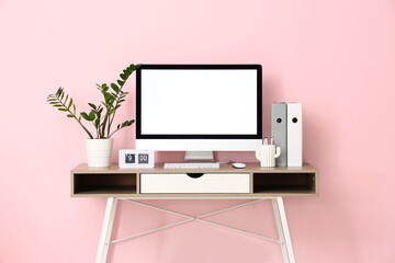Stylish workplace with modern computer, houseplant and clock near pink wall in office