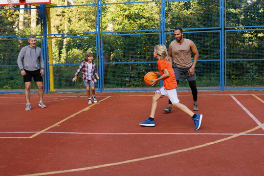 Father and sons playing basketball with trainer on outdoor court
