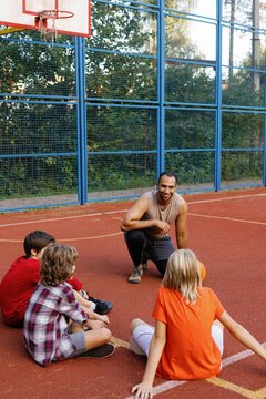 Trainer instructing students on outdoor basketball court during break