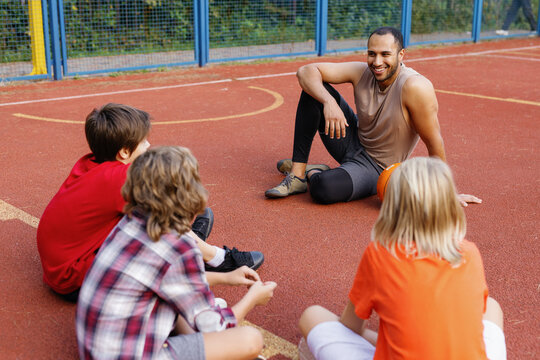 PE teacher resting with his pupils on basketball court during break