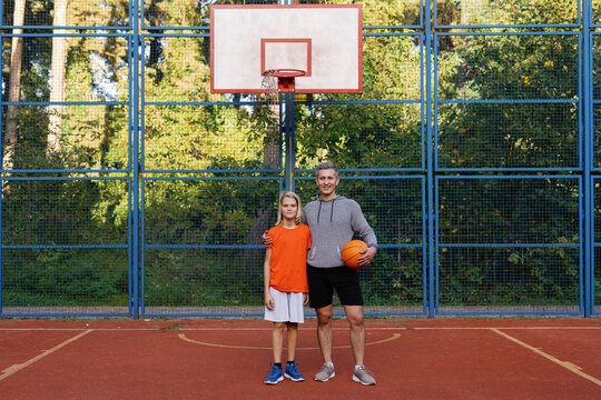 Father posing with son in front of basketball hoop on outdoor court