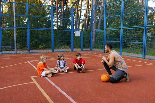 PE teacher instructing schoolboys on court during basketball workout