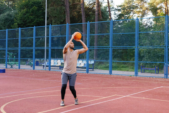 Basketball coach performing set shot on outdoor court during training