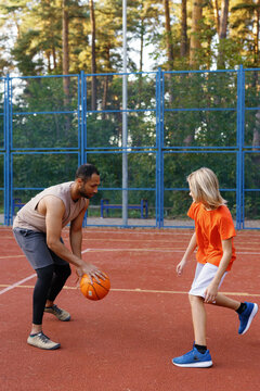 Basketball trainer teaching his student how to dribble ball on court
