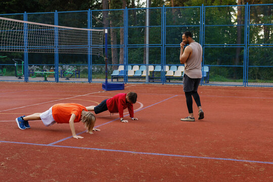 Sports coach watching boys performing push-ups on basketball court