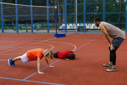 Kid and his teammate trying to do plank supervised by basketball coach