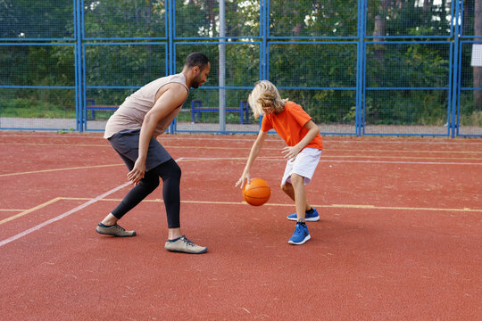 Student dribbling ball on court during workout with personal trainer