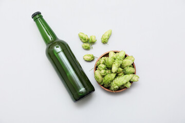 Bowl with green hops cones and bottle of beer on white background