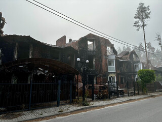 Naklejka premium Hostomel, Kyiv region, shrouded in morning fog, reveals a haunting scene of burnt-out homes and vehicles, remnants of recent devastation. The mist adds an eerie calm to the aftermath of conflict.