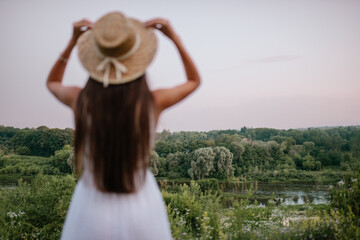 Obraz premium A woman is beautifully embracing nature while wearing a straw hat and a flowing dress,