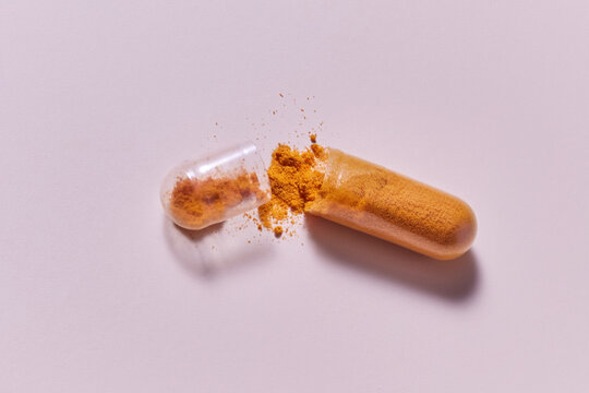 Split transparent capsule with orange dust scattered in studio
