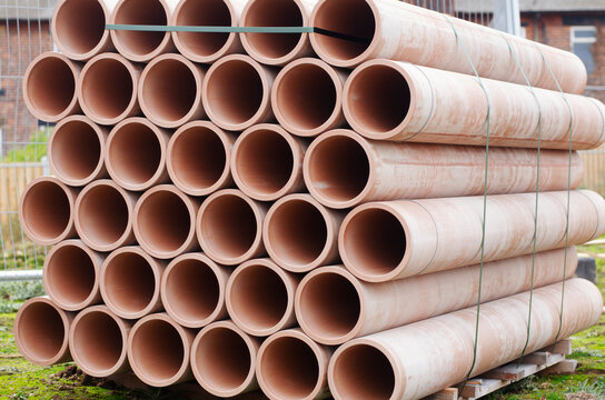 Stacked terracotta cly ceramic drainage pipes ready for installation at a construction site during daylight hours