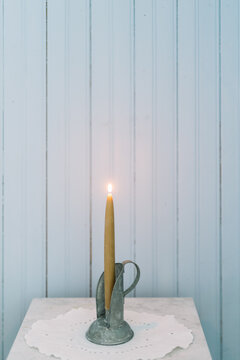 Candle on a table with white doily in front of wall.