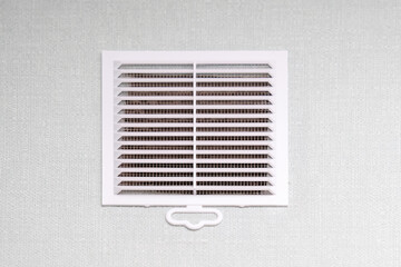 A rectangular white air vent is hanging on an equally white wall