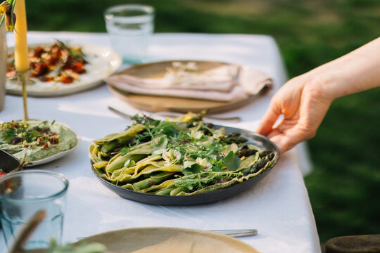 Hand placing a dish of greens on a set dining table