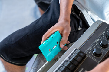 Hand holding a teal cassette tape near a vintage boombox