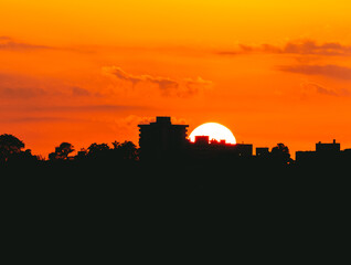 Fototapeta premium A Vibrant Sunset Over A City Skyline With Silhouetted Buildings And Trees, Casting A Beautiful Glow That Highlights The Urban Landscape And Creates A Stunning Evening Atmosphere.