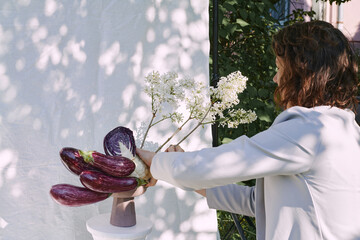 A woman arranges eggplants and flowers in a unique display outdoors