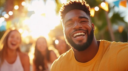 Obraz premium A cheerful man in a bright yellow shirt is laughing under the sun at an outdoor celebration, surrounded by friends with a background of colorful decorations.