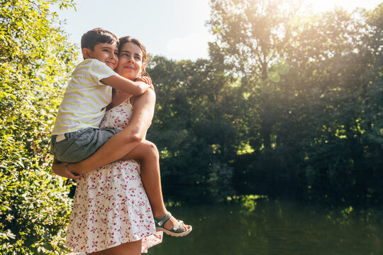 Mother embracing son outdoors with sunlit trees in background